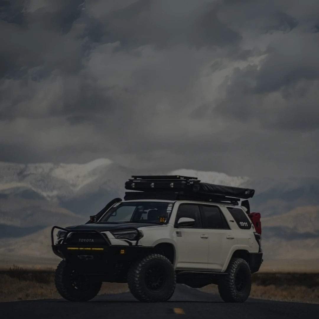 A white Toyota 4Runner built for remote exploration stands on an open mountain road under stormy skies, equipped with toyota off-road parts and 4runner accessories.