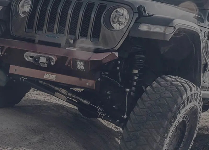 Close-up of a modified Jeep front end with aggressive tires and aftermarket bumper, showcasing jeep jk off road parts and american made jeep parts on rocky terrain.