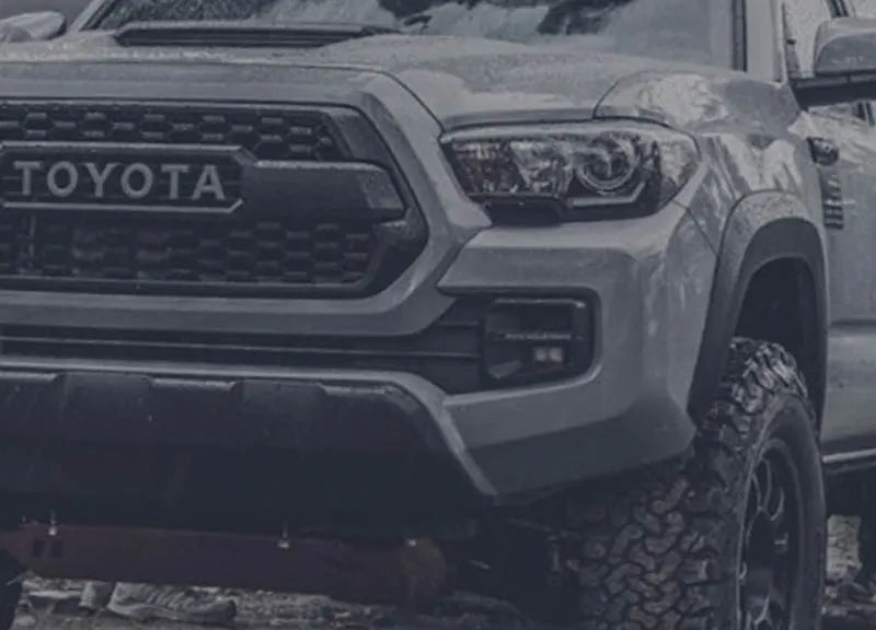 Front view of lifted Toyota Tacoma parked on a forest trail, equipped with toyota tacoma accessories and rugged toyota off-road parts for serious overlanding use.